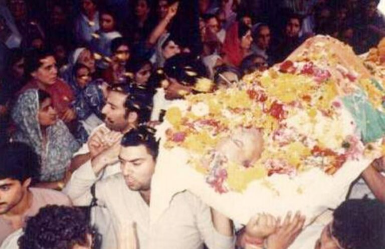 Funeral procession of Tika Lal Taploo, showing a large crowd surrounding a flower-covered body being carried by mourners